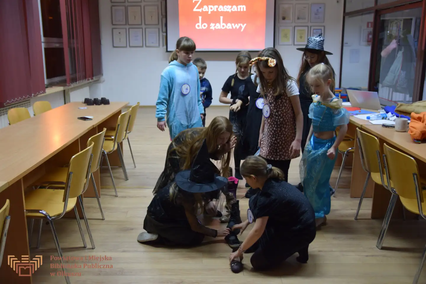 Zdjęcie zostało zrobione w trakcie zabaw andrzejkowych. Przedstawia grupę dzieci, które ustawiają buty w linii prostej.