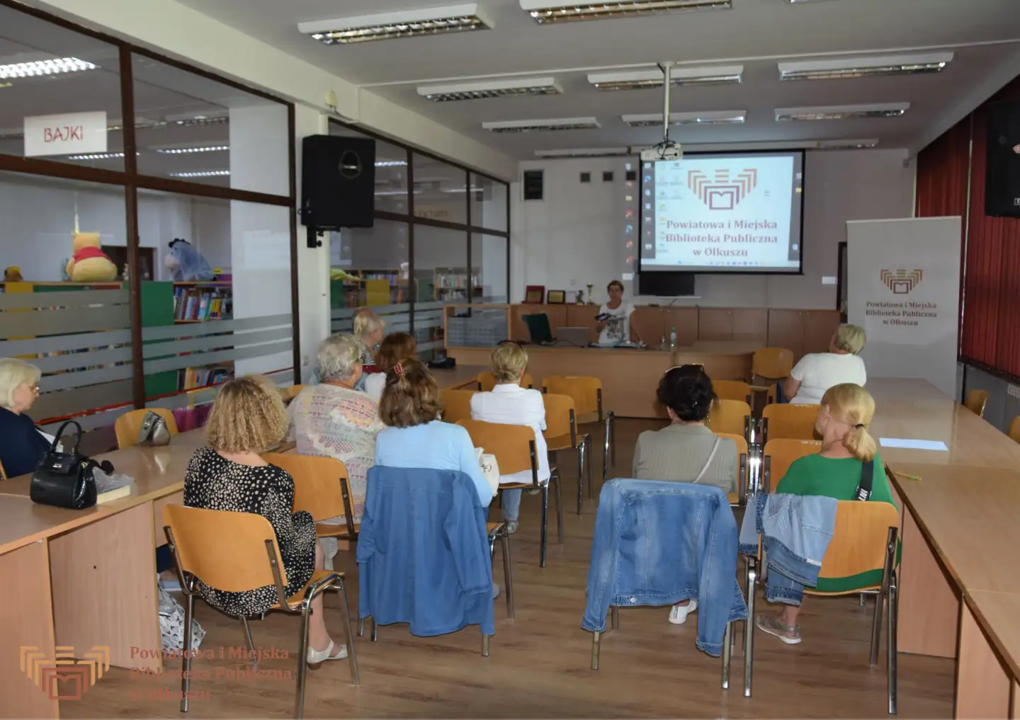 Grupa kobiet siędząca na krzesłach w sali konferencyjnej w trakcie prezentacji